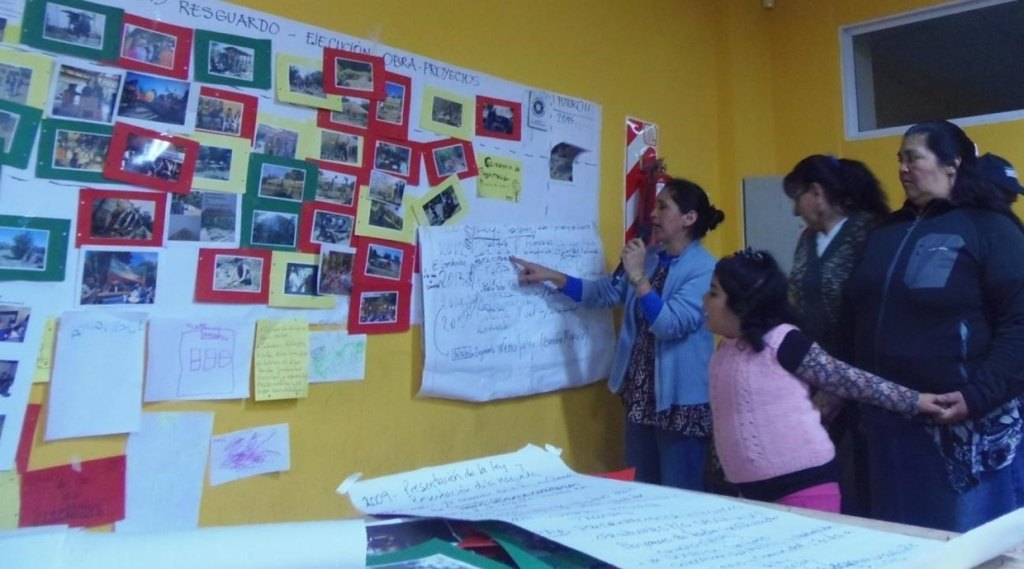 Taller del proceso del Barrio Intercultural Sustentable, Comunidad de Cambio: vecinas trabajan frente a un mural de fotos y papelógrafos